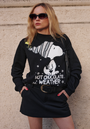 Eine Frau mit Sonnenbrille und einem schwarzen "HOT CHOCOLATE WEATHER" Snoopy-Pullover von Princess Goes Hollywood steht vor einer beigefarbenen, strukturierten Wand. Sie trägt dazu einen kurzen Rock, eine schwarze Umhängetasche und hält ihre Hände in den Taschen.