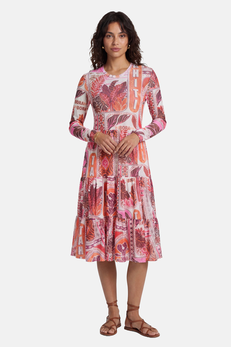 Eine Frau mit welligem braunem Haar trägt ein farbenfrohes „Princess Goes Hollywood“-Mesh-Kleid mit einem lebhaften Tahiti-Print (rosa, orange, rot) und Aufschriften wie „HILO“ und „BORA BORA“. Das knielange Kleid wird vor einem weißen Hintergrund mit braunen Sandalen kombiniert.