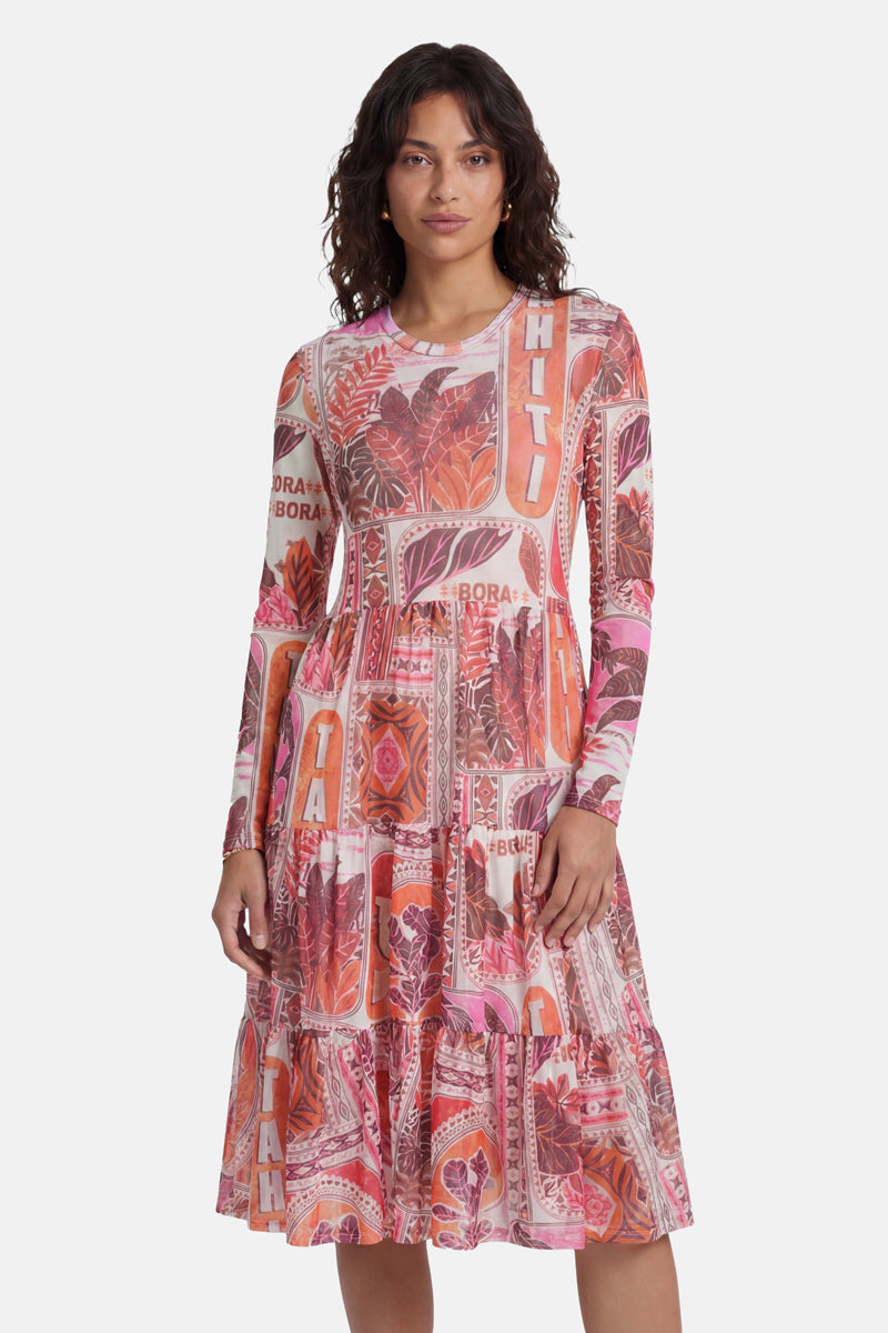 Eine Frau mit welligem, dunklem Haar trägt ein langärmeliges, knielanges Netzkleid der Marke „Princess Goes Hollywood“ mit einem leuchtenden Tahiti-Print (in Rosa, Orange und Weiß), das sich durch ein figurbetontes Oberteil, einen gestuften Rock und ein Unterkleid auszeichnet, und steht vor einem weißen Hintergrund.