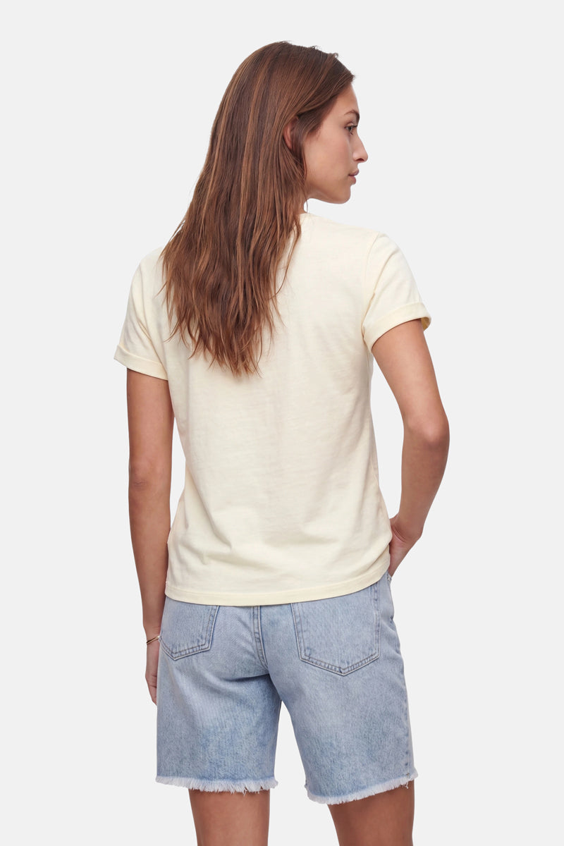 Eine Frau mit langen braunen Haaren steht mit dem Rücken zur Kamera und trägt ein hellgelbes Baumwoll-T-Shirt der „Frogbox by Princess Limited Edition“ sowie hellblaue Jeansshorts. Ihr linker Arm ruht an ihrer Seite vor einem schlichten weißen Hintergrund.