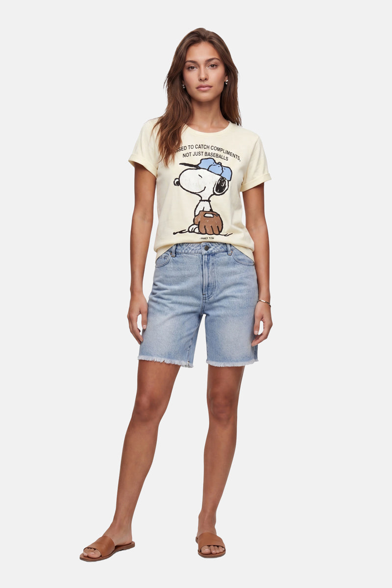 Eine Frau blickt nach vorne und trägt ein hellgelbes „Frogbox by Princess Snoopy“-T-Shirt aus Baumwolle, hellblaue Jeansshorts und braune Pantoletten. Ihr offenes braunes Haar und ihr entspannter, selbstbewusster Blick heben sich von einem schlichten weißen Hintergrund ab.