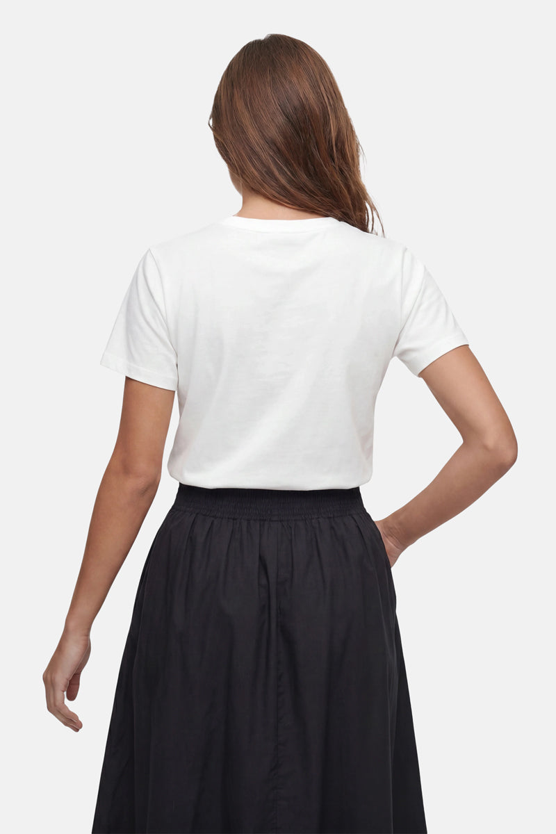 Eine Frau mit langen braunen Haaren, die der Kamera den Rücken zukehrt, trägt ein „Frogbox by Princess Limited Edition Snoopy“-T-Shirt aus Baumwolle, das in einen schwarzen Rock mit hoher Taille gesteckt ist, vor einem einfarbigen hellgrauen Hintergrund.