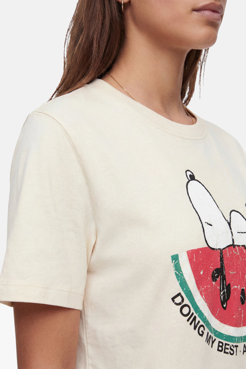 Eine Frau mit braunen Haaren trägt ein cremefarbenes T-Shirt der Marke „Frogbox by Princess Baumwolle“ mit einem Schmetterling auf einer Wassermelonenscheibe und der Aufschrift „DOING MY BEST“. Vor einem einfarbigen Hintergrund sind nur ihr unteres Gesicht und ihr Oberkörper zu sehen.