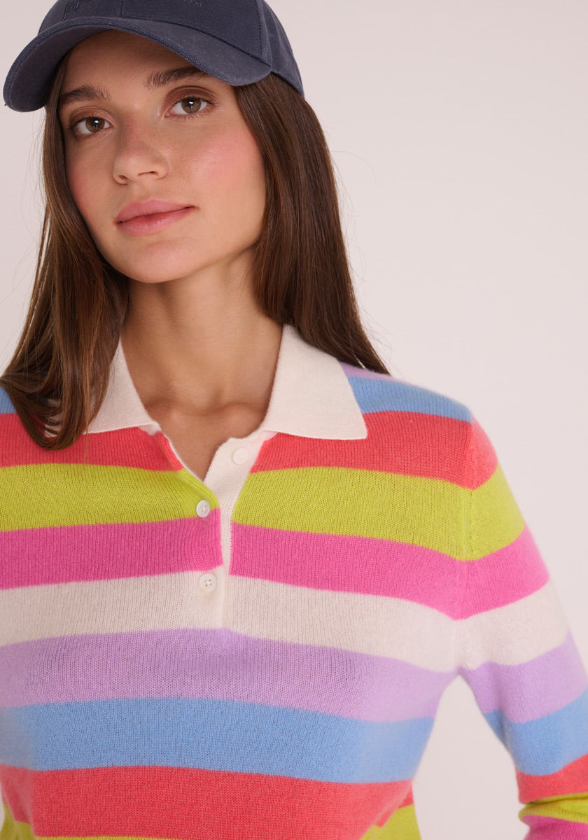 Eine Frau mit einer marineblauen Baseballmütze trägt einen Princess Goes Hollywood Feinstrickpullover mit breiten, bunten Streifen, Knöpfen am Hals und einem Polokragen. Sie hat glattes braunes Haar und einen neutralen Gesichtsausdruck.