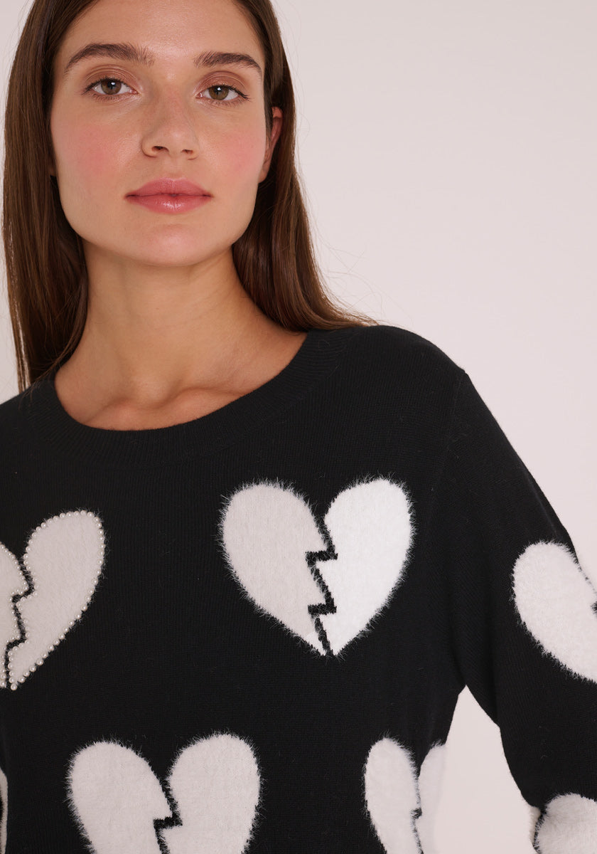 Eine Frau mit langen braunen Haaren trägt einen Princess Goes Hollywood Wollmix Pullover mit Rundhalsausschnitt und auffälligem weißen Herz-Motiv. Im Brustbereich abgeschnitten, posiert sie neutral vor einem schlichten, hellen Hintergrund.