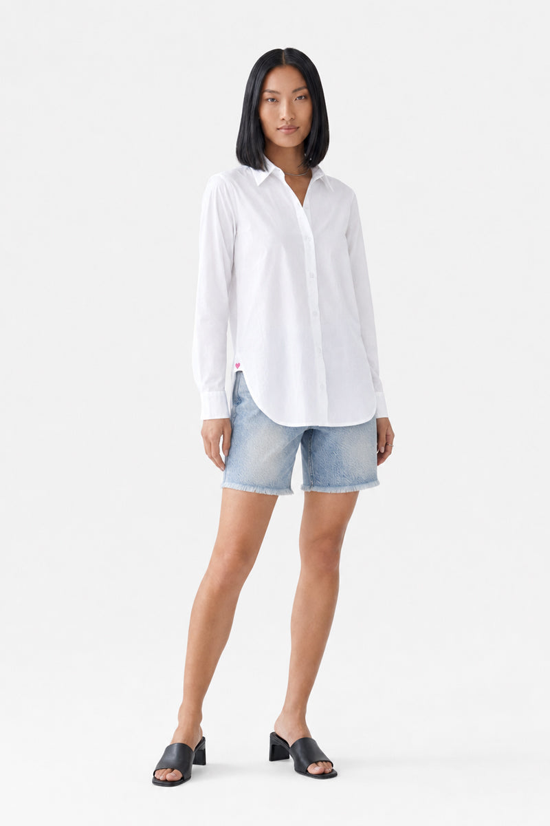 Eine Frau mit glattem schwarzem Haar präsentiert eine langärmelige weiße Hemdbluse aus Baumwolle von Princess Goes Hollywood, kombiniert mit hellblauen Jeansshorts und schwarzen Pumps mit offener Spitze. Sie steht mit dem Gesicht nach vorne vor einem schlichten weißen Hintergrund und blickt mit neutralem Gesichtsausdruck in die Kamera.