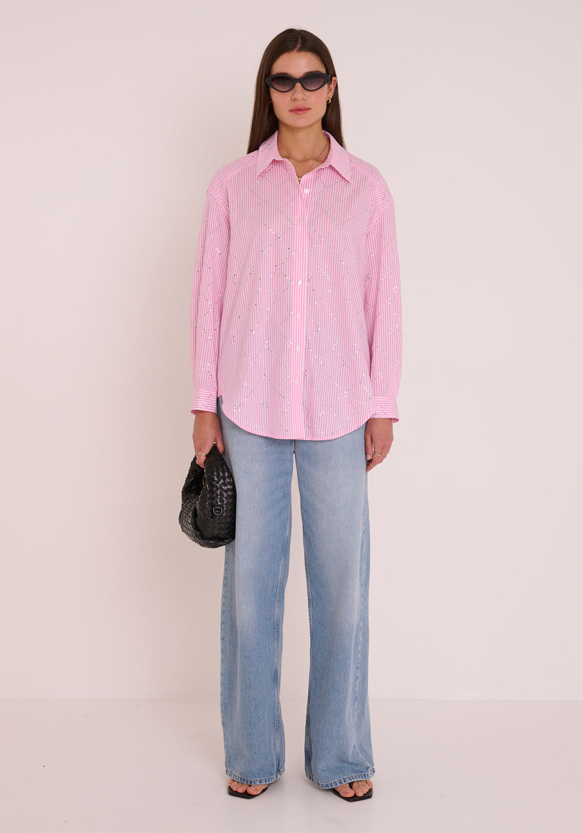 Eine Frau steht vor einem schlichten weißen Hintergrund und trägt ein gestreiftes Baumwollhemd von Princess Goes Hollywood in zartem Rosa, weite hellblaue Jeans, schwarze Sandalen mit offenen Zehen, eine dunkle Sonnenbrille und eine kleine schwarze strukturierte Handtasche.