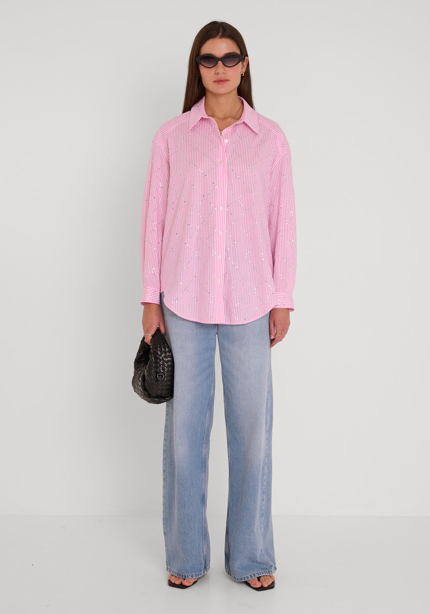 Eine Frau in einem gestreiften Baumwollhemd von Princess Goes Hollywood, hellblauen, weit geschnittenen Jeans und schwarzen Sandalen steht vor einem weißen Hintergrund. Sie hat glattes braunes Haar, eine dunkle Sonnenbrille und trägt eine schwarze Handtasche mit Struktur.