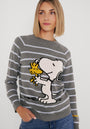 Eine Frau mit glattem blondem Haar trägt einen Princess Goes Hollywood gestreifter Baumwollmix-Pullover mit großem Snoopy-Woodstock-Print. Sie lächelt sanft, steht vor einem weißen Hintergrund und hat eine Hand in ihrer Jeanstasche.