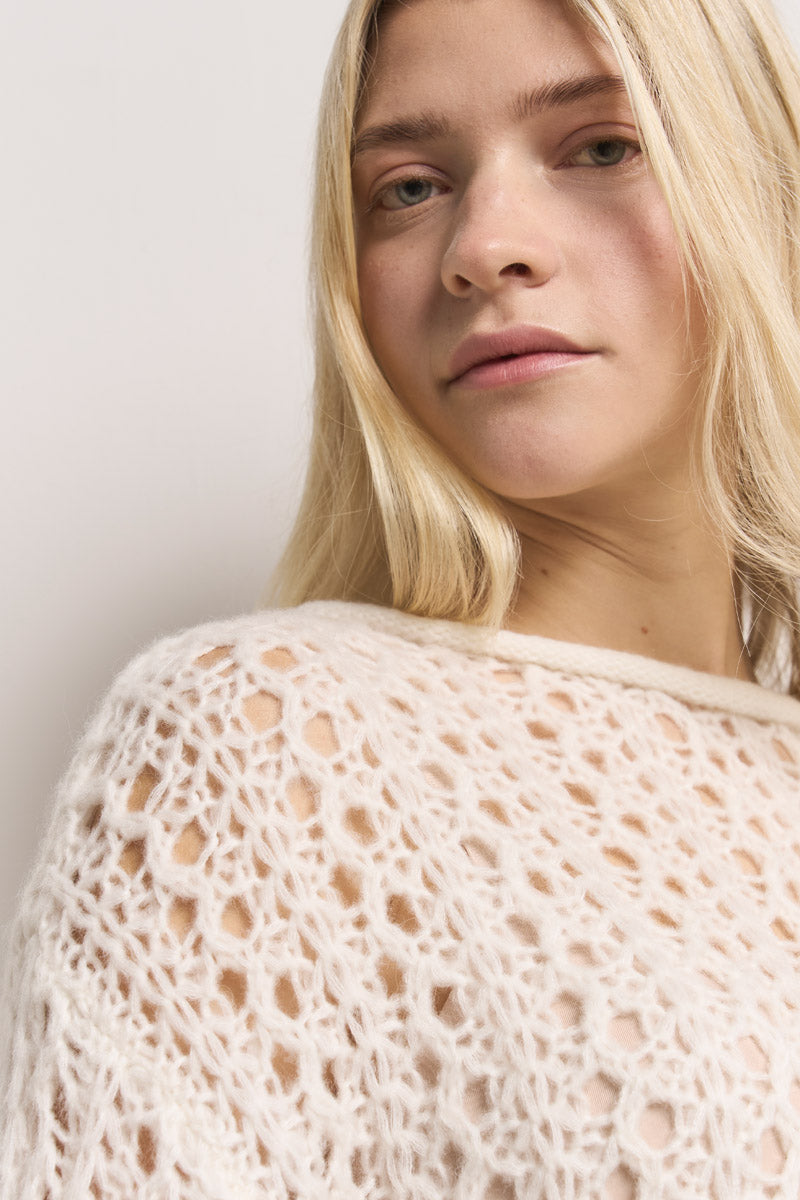 Eine junge Frau mit langen blonden Haaren blickt nach oben und trägt einen strukturierten Princess Goes Hollywood Damen Pullover mit einem eleganten, offenen Blumenmuster aus Spitze. Der unifarbene Hintergrund hebt ihr heiteres Gesicht und den raffinierten Ajourstrick-Stoff hervor.