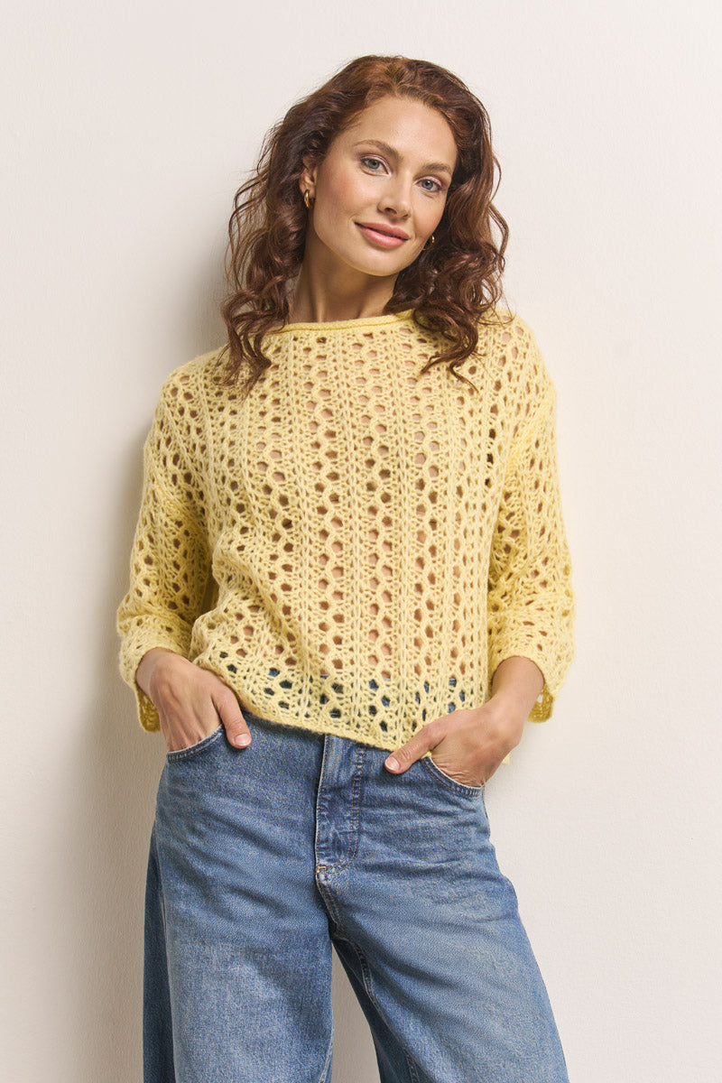 Eine Frau mit langen, gewellten roten Haaren steht vor einer cremefarbenen Wand und lächelt sanft in die Kamera. Sie trägt einen locker sitzenden Princess Goes Hollywood Ajourstrick-Pullover aus weichem Merino-Alpaka-Mix und eine Bluejeans mit hoher Taille, die Hände in den Taschen.