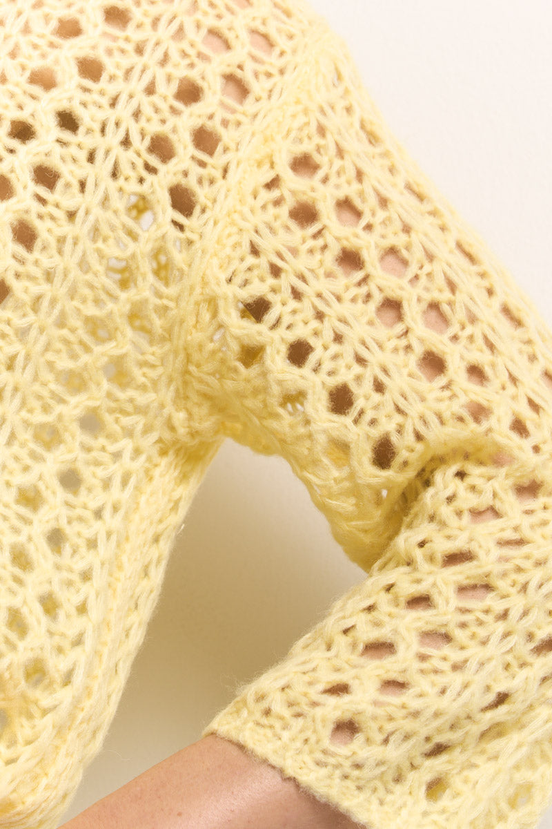 Nahaufnahme des Arms einer Person in einem langärmeligen, hellgelben Ajourstrick-Pullover von Princess Goes Hollywood mit zartem Spitzenmuster und luftiger, durchsichtiger Textur, wobei der Schwerpunkt auf dem Ärmel und dem Oberarm vor einem unifarbenen Hintergrund liegt.