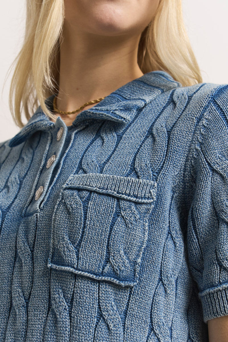 Nahaufnahme einer Frau, die einen hellblauen Princess Goes Hollywood Zopfstrick-Baumwollpullover mit Kragen, Knöpfen vorne und Brusttasche trägt. Sie trägt außerdem eine goldene Halskette. Das Bild ist auf ihren Hals, ihre Schultern und ihren Oberkörper zugeschnitten.