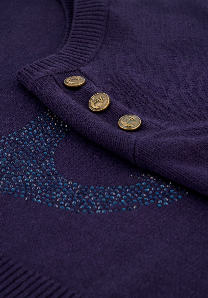 Nahaufnahme eines dunkelvioletten Princess Goes Hollywood-Pullovers aus einer Baumwollmischung mit drei goldenen Ankerknöpfen am Kragen und blauen Strassverzierungen, die unterhalb des Kragens ein teilweise geschwungenes Muster bilden.