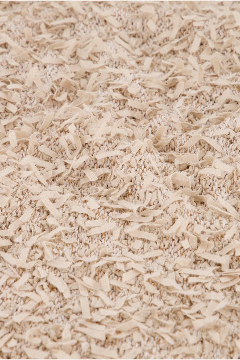 Nahaufnahme eines beigefarbenen Strukturteppichs mit zotteligen, unregelmäßigen Stoffstreifen, die über die gesamte Oberfläche gewebt sind und an einen Princess Goes Hollywood Effektgarn-Pullover erinnern. Die einheitliche hellbraune Farbe verleiht ihm ein gemütliches, warmes Aussehen.