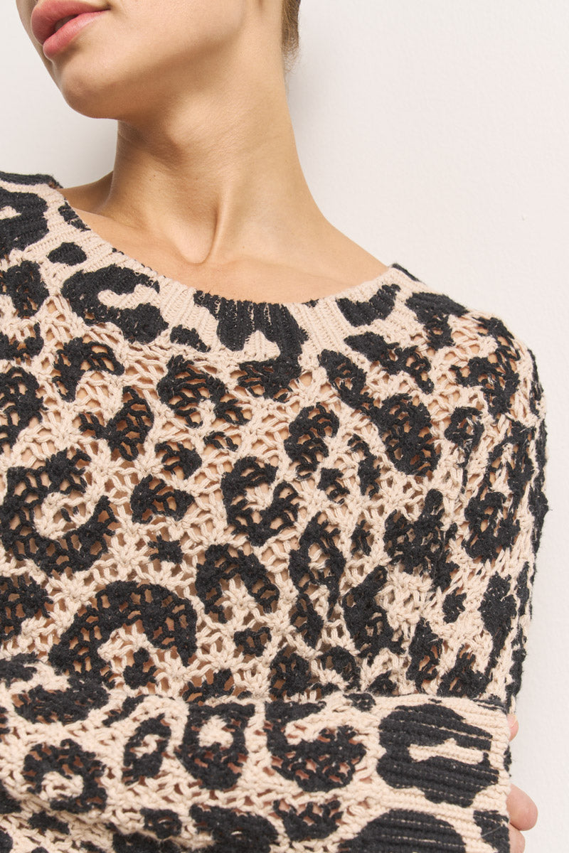 Eine Nahaufnahme zeigt eine Person, die einen beigen Häkelpullover mit Leo-Print aus 100 % Baumwolle von Princess Goes Hollywood trägt, wobei das untere Gesicht, der Hals und der Oberkörper vor einem einfarbigen hellen Hintergrund hervorgehoben werden.