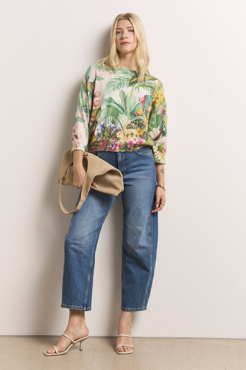 Eine Frau mit langen blonden Haaren steht vor einer schlichten Wand. Sie trägt einen Princess Goes Hollywood Jungle-Print Pullover mit Baumwollanteil mit 3/4-Ärmel, blaue Jeans mit Bündchen, beigefarbene Sandalen mit Absatz und eine beigefarbene Umhängetasche. Sie sieht entspannt aus und hat eine Hand in der Tasche.