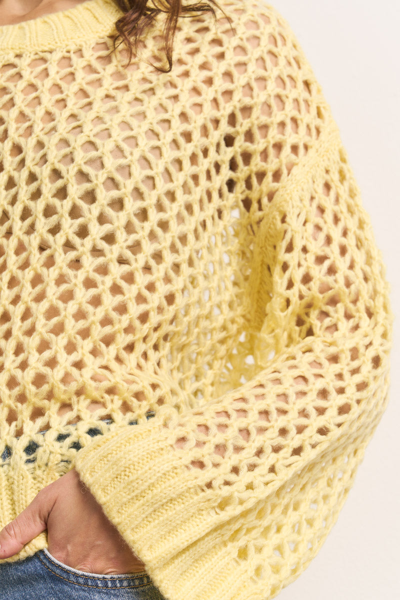 Nahaufnahme einer Person, die einen gelben Grobstrickpullover von Princess Goes Hollywood mit breitem Lochstrick-Muster trägt. Der Pullover aus Merino-Alpaka-Mix hat dicke Rippbündchen an den Ärmeln und am Saum, darunter ist teilweise eine blaue Jeans zu sehen.