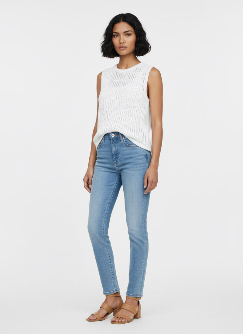 Eine Frau mit kurzen schwarzen Haaren trägt einen Princess Goes Hollywood ärmellosen Lochstrick-Pullunder aus Baumwolle mit Rundhalsausschnitt, hellblaue Skinny Jeans und hellbraune Sandalen. Sie steht vor einem schlichten weißen Hintergrund, entspannt und leicht nach links gewandt.