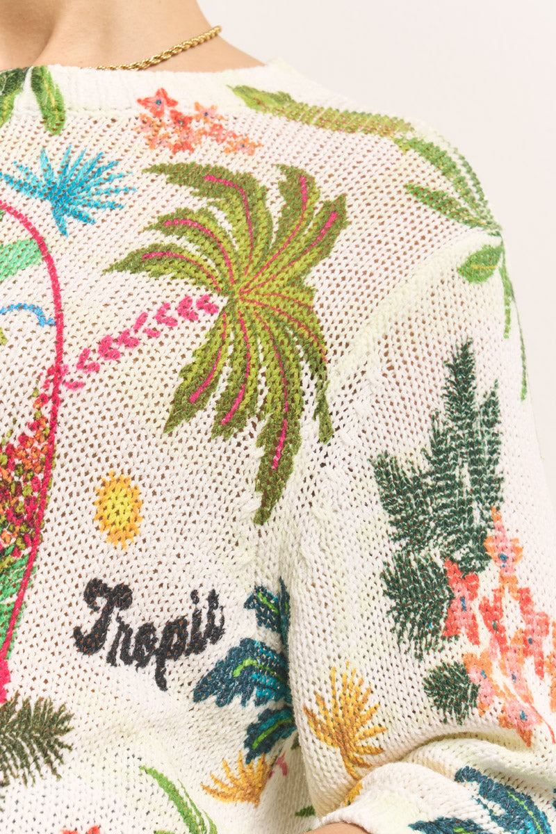 Nahaufnahme eines gestrickten cremefarbenen Princess Goes Hollywood-Pullovers mit bunten gestickten tropischen Pflanzen, Palmen, Blättern und Blumen. Der Schriftzug "Tropii" ist in schwarzer Schrift aufgestickt, am Halsausschnitt befindet sich eine goldene Halskette.