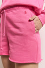Eine Nahaufnahme zeigt eine Person in der Princess Goes Hollywood Sweatshorts in leuchtendem Pink mit rohem Saum, elastischem Bund, passendem Kordelzug und weichem Stoff aus 100 % Baumwolle, gepaart mit einem passenden rosa Oberteil für einen bequemen Look.
