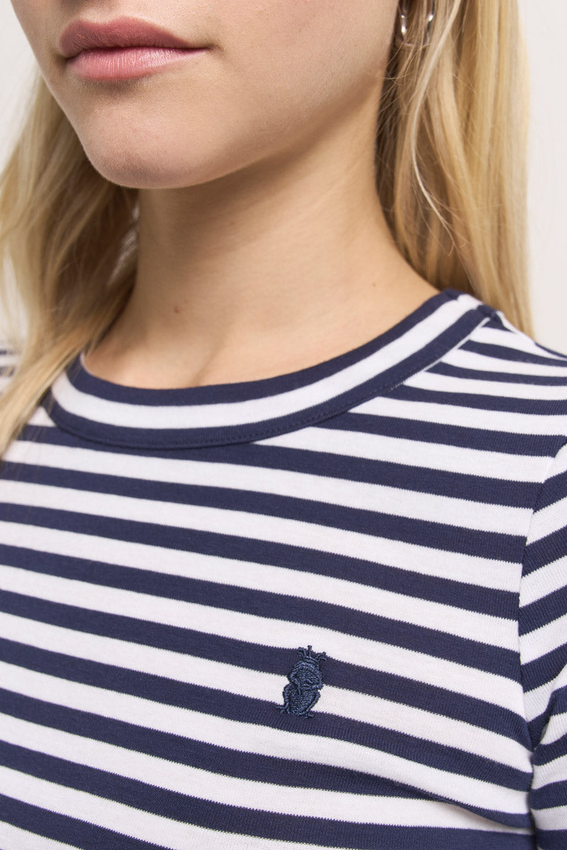 Nahaufnahme einer Frau, die ein marineblau-weiß gestreiftes Baumwoll-T-Shirt von Princess Goes Hollywood mit einem kleinen gestickten Seepferdchen-Logo auf der Brust trägt. Ihre helle Haut und ihr langes blondes Haar umrahmen ihr unteres Gesicht und ihren oberen Oberkörper, die sichtbar sind.