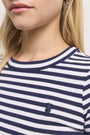 Nahaufnahme einer Frau, die ein marineblau-weiß gestreiftes Baumwoll-T-Shirt von Princess Goes Hollywood mit einem kleinen gestickten Seepferdchen-Logo auf der Brust trägt. Ihre helle Haut und ihr langes blondes Haar umrahmen ihr unteres Gesicht und ihren oberen Oberkörper, die sichtbar sind.