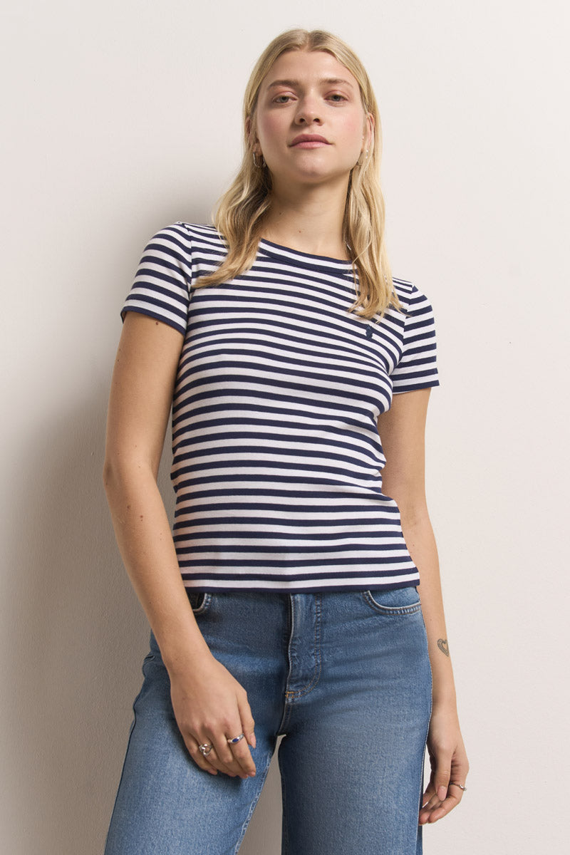 Eine junge Frau mit langen blonden Haaren steht vor einer weißen Wand. Sie trägt ein marineblau-weiß gestreiftes Baumwoll-T-Shirt von Princess Goes Hollywood und blaue Jeans. Sie blickt selbstbewusst, mit neutralem Gesichtsausdruck und entspannter Körperhaltung in die Kamera.