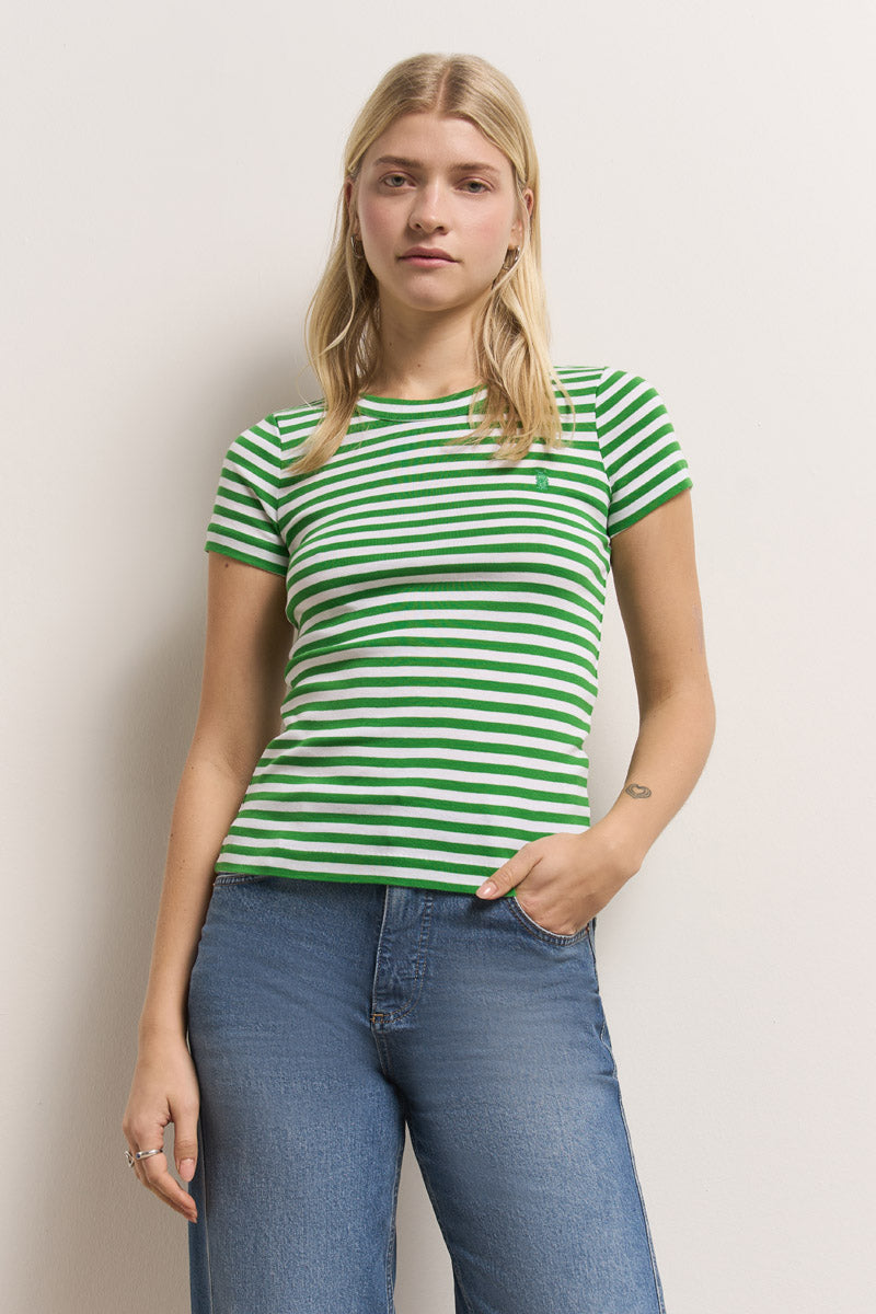 Eine junge Frau mit langen blonden Haaren trägt ein Princess Goes Hollywood gestreiftes Baumwoll-T-Shirt und Blue Jeans und steht vor einer schlichten hellen Wand. Sie blickt ruhig in die Kamera, eine Hand in der Tasche, die andere entspannt an der Seite.