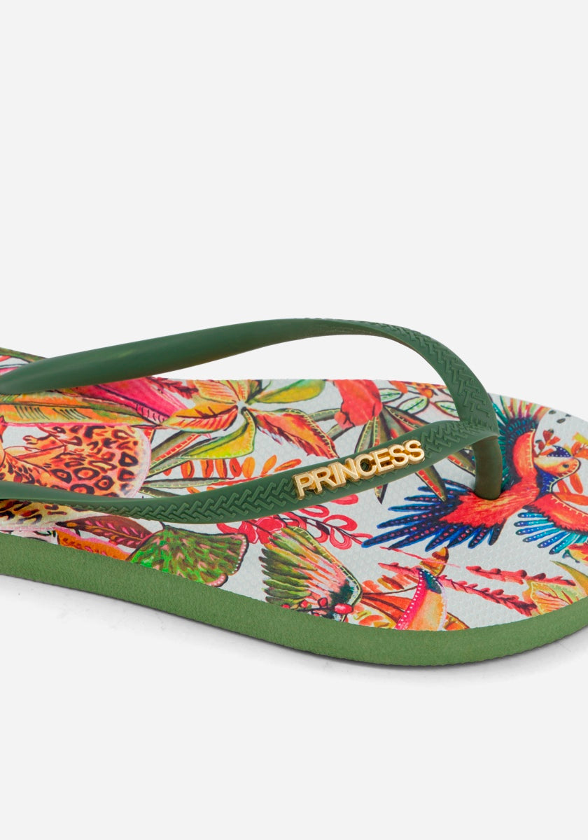 Eine Nahaufnahme eines Princess Goes Hollywood Flip Flops mit grünen Riemen, einem lebhaften tropischen Dschungeldruck mit Blumen und Vögeln auf der Sohle und "PRINCESS" in goldenen Buchstaben auf einem Riemen - ein ideales Sommeraccessoire auf weißem Hintergrund.