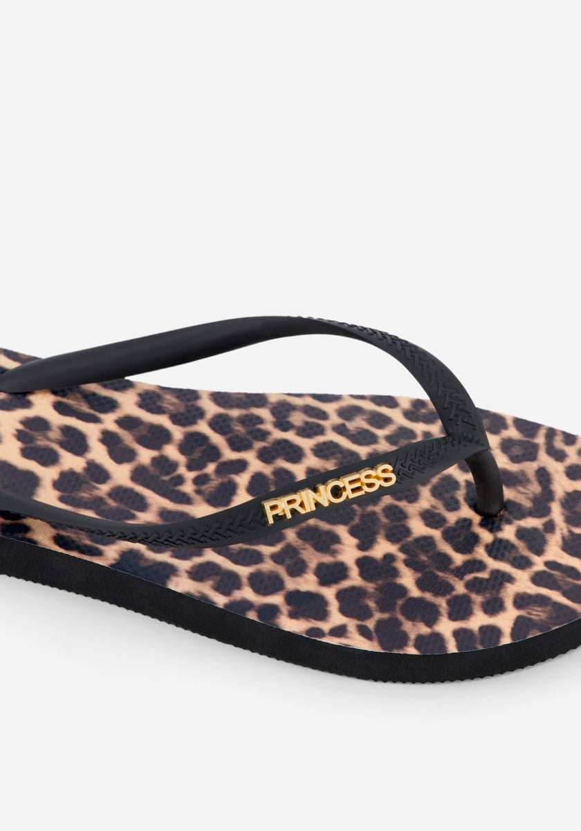 Eine Nahaufnahme der Princess Goes Hollywood Leopardenmuster Flip Flops mit einem schwarzen Riemen mit goldener PRINCESS-Prägung, einem hellbraunen und dunkelbraunen Leopardenmuster und einer schwarzen Sohle - die perfekten sommerlichen Sandalen.