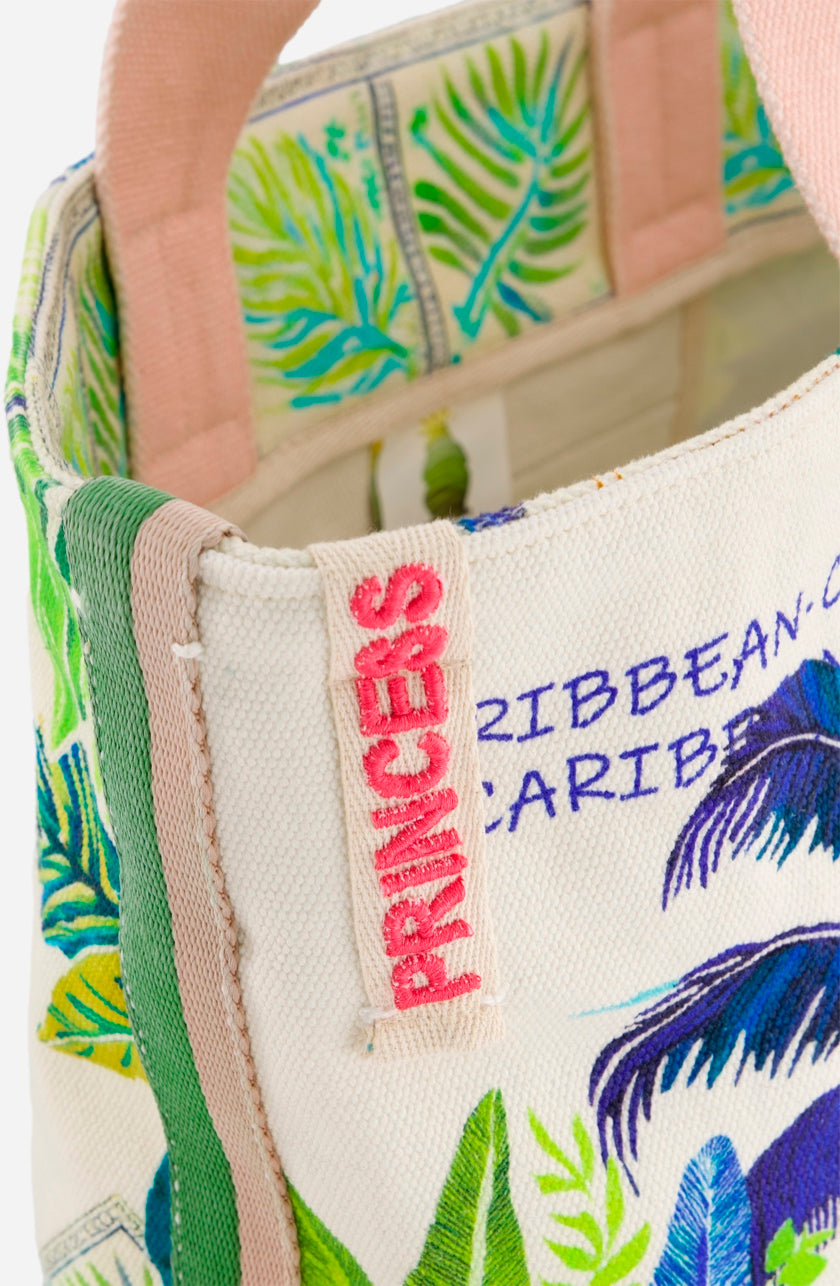 Eine Nahaufnahme einer farbenfrohen Strandtasche aus Baumwollstoff von Princess Goes Hollywood mit tropischen Blattmustern in Grün, Blau und Gelb, einem dicken rosafarbenen Griff, dem PRINCESS-Anhänger und dem Schriftzug CARIBBEAN" - ideal für Ausflüge nach St-Barth.