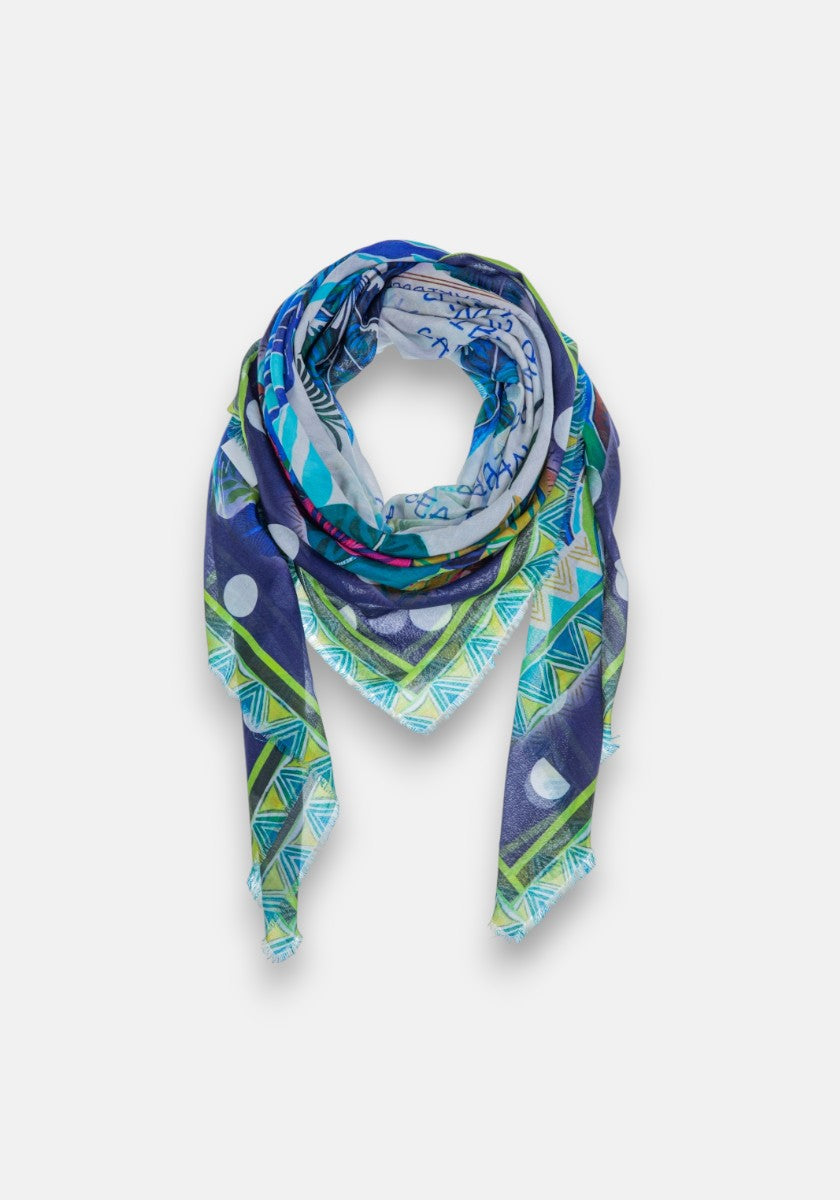 Ein leuchtendes Dreieckstuch von Princess Goes Hollywood im Baumwolle-Modal-Mix mit geometrischen und abstrakten St. Barth-Print-Mustern in Blau, Grün, Lila und Weiß, stilvoll geschlungen, um sein farbenfrohes Design zu präsentieren.