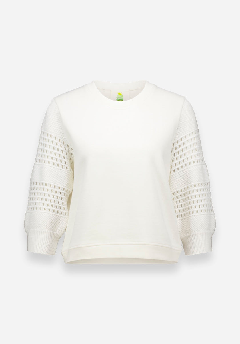 Der weiße Pullover Princess Goes Hollywood für Damen hat einen Rundhalsausschnitt, spitzenähnliche Strickmuster auf Dreiviertel-Ärmeln, die von der Lochstickerei inspiriert sind, und einen schlichten, leicht kastenförmigen Körper aus weicher Baumwolle. Vor einem hellgrauen Hintergrund.