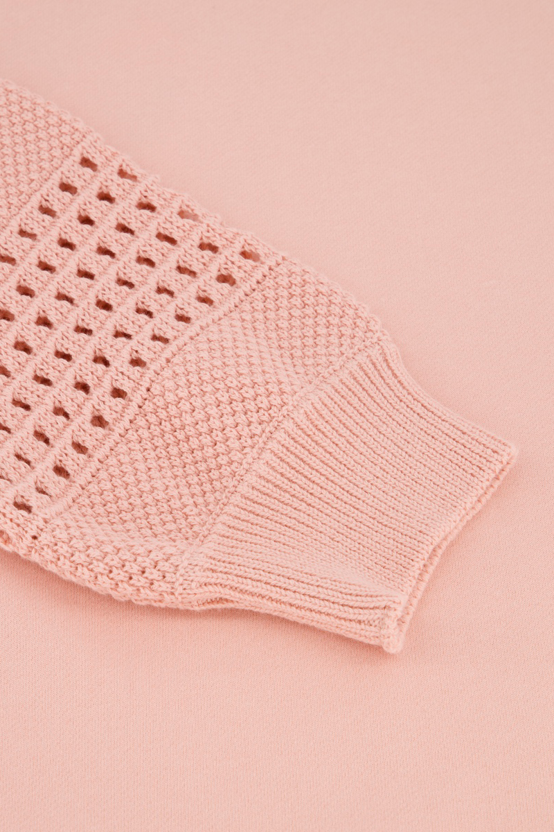 Nahaufnahme eines hellrosa Princess Goes Hollywood Baumwollstrickpullover-Ärmels mit Strukturmuster, offenen Strickabschnitten und Rippenbündchen, dargestellt auf einem flachen, passenden rosa Hintergrund.