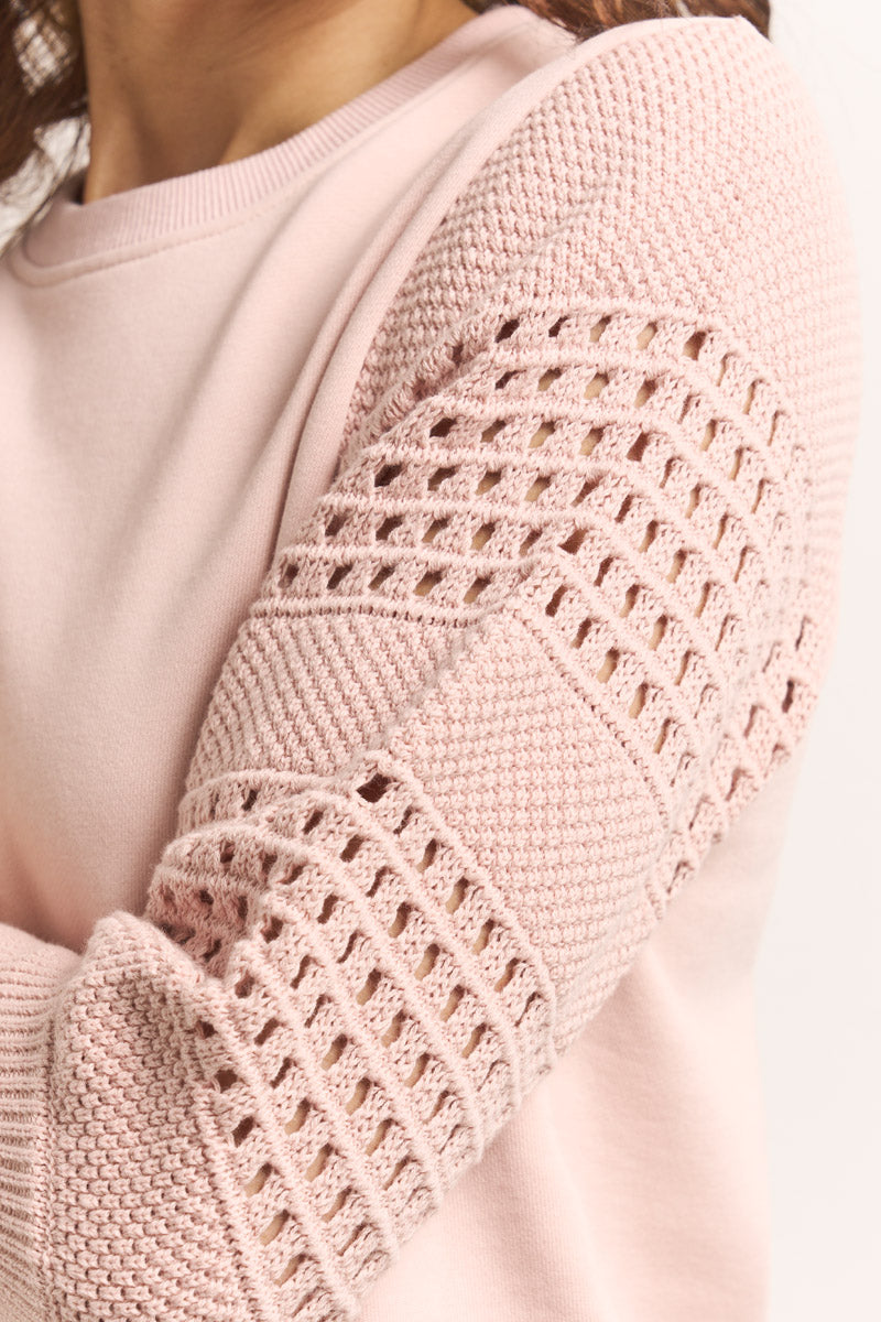 Nahaufnahme einer Person, die ein Princess Goes Hollywood Sweatshirt aus hellrosa Baumwolle trägt. Die 3/4-Ärmel weisen ein kompliziertes Strickmuster mit offenem Gitterwerk und strukturierten Abschnitten auf, die für dekorativen Stil sorgen. Der Rundhalsausschnitt unterstreicht den weichen, bequemen Look.