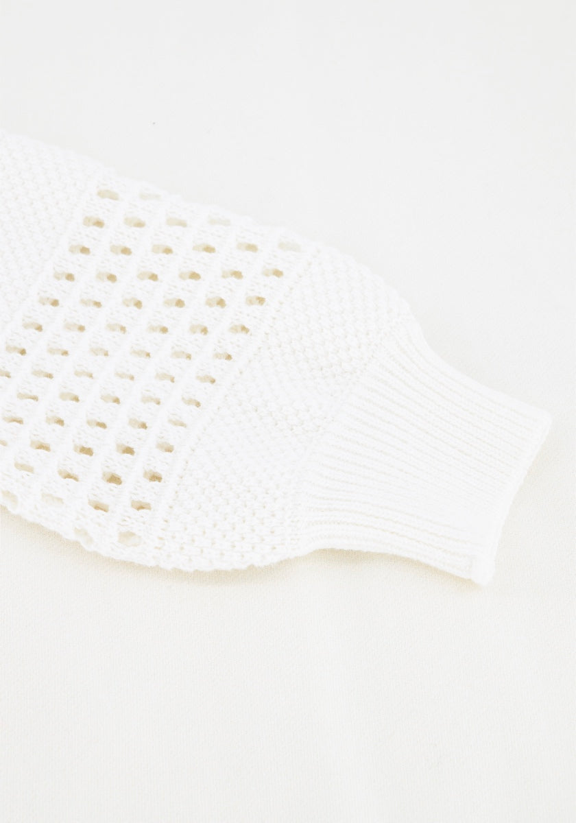 Eine Nahaufnahme eines weißen Princess Goes Hollywood Baumwolle-Ärmels zeigt ein geripptes Bündchen und eine luftige Lochstickerei. Der dichte Strick am Bündchen kontrastiert mit dem Lochmuster auf dem Körper, das vor einem schlichten weißen Hintergrund steht.