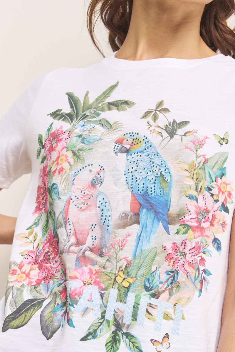 Ein weißes Baumwoll-T-Shirt von Princess Goes Hollywood zeigt einen leuchtenden Papagei-Print mit zwei Papageien - einer rosa, einer blau - inmitten von tropischen Blumen und grünen Blättern sowie "A.HITI" in großen hellblauen Buchstaben am unteren Rand.