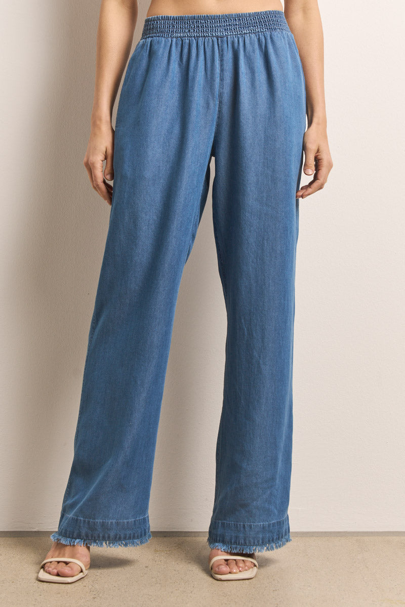 Eine Person steht vor einer hellen Wand und trägt weite Lyocell-Hose von Princess Goes Hollywood mit Smokbund und fransigen Säumen. Die Hände stecken in den Seitentaschen, sie tragen offene Sandalen. Sichtbar ist nur die untere Körperhälfte.