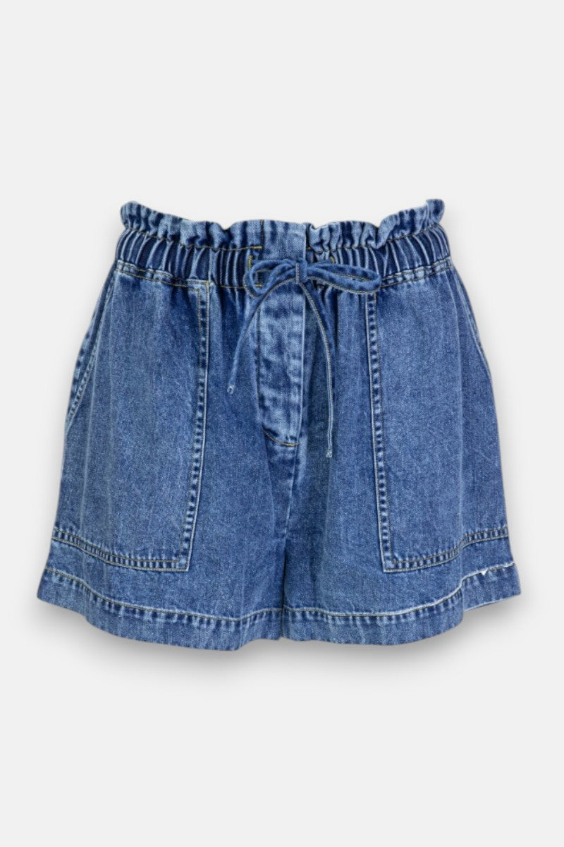 Princess Goes Hollywood ist eine blaue Jeansshorts mit hoher Taille aus weichem Baumwoll-Denim. Sie hat eine geraffte Paperbag-Taille mit Kordelzug, große aufgesetzte Taschen vorne, sichtbare Nähte und eine lockere, leicht ausgestellte Passform. Hintergrund: einfarbig hellgrau.