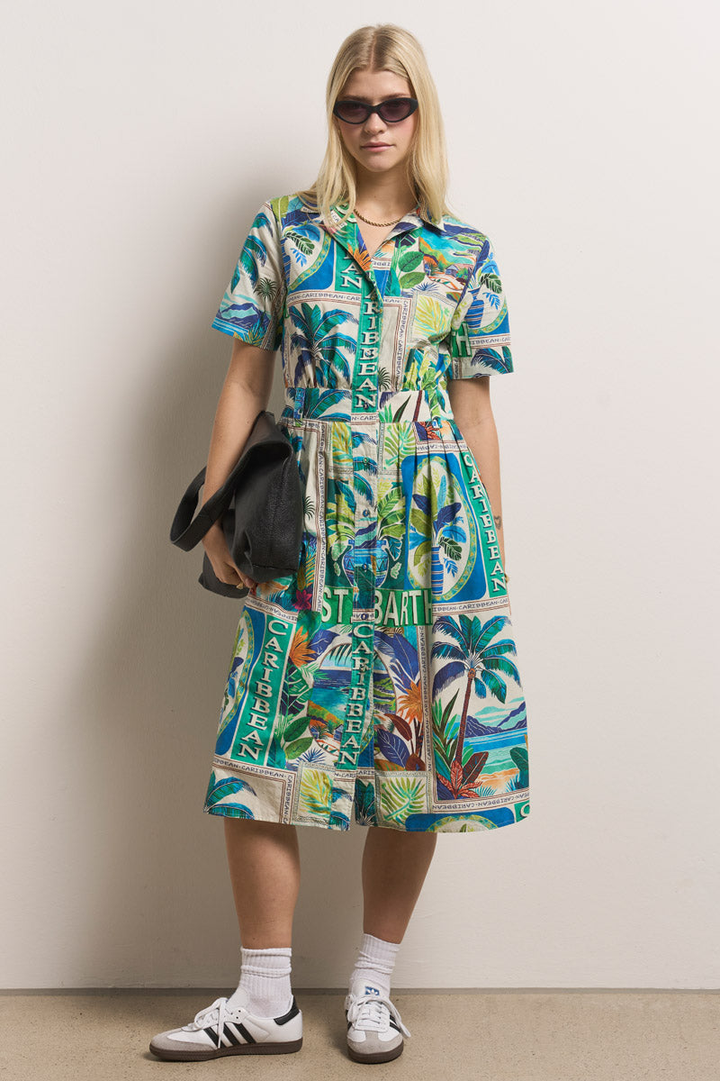 Eine Frau mit langen blonden Haaren trägt eine schwarze Sonnenbrille, ein buntes Princess Goes Hollywood St. Barth-Print Midikleid aus Baumwolle, weiße Socken und Adidas-Turnschuhe. Sie hält eine schwarze Handtasche in der Hand, steht an einer weißen Wand und schaut ruhig in die Kamera.