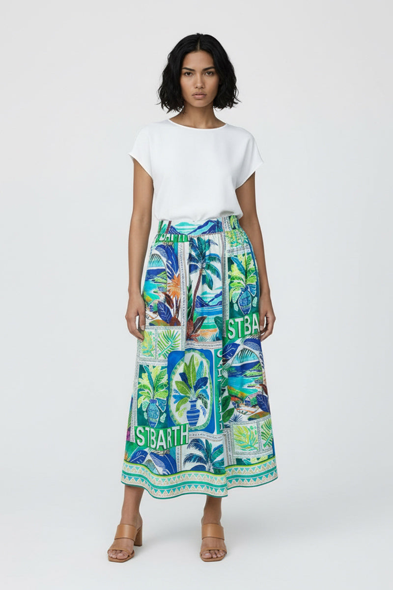 Eine Frau mit kurzen dunklen Haaren trägt ein weißes kurzärmeliges Oberteil und einen farbenfrohen Princess Goes Hollywood Midirock aus Baumwolle mit lebhaftem St. Barth-Print und Palmen, gepaart mit hellbraunen Sandalen mit Absatz vor einem schlichten hellen Hintergrund.