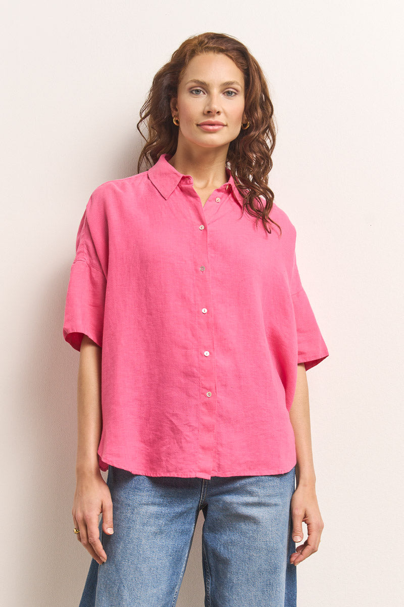 Eine Frau mit gewelltem braunem Haar trägt eine hellrosa Oversize-Bluse mit Hemdkragen von Princess Goes Hollywood und hellblaue Jeans. Sie steht vor einem cremefarbenen Hintergrund und blickt selbstbewusst und mit einem leichten Lächeln in die Kamera.