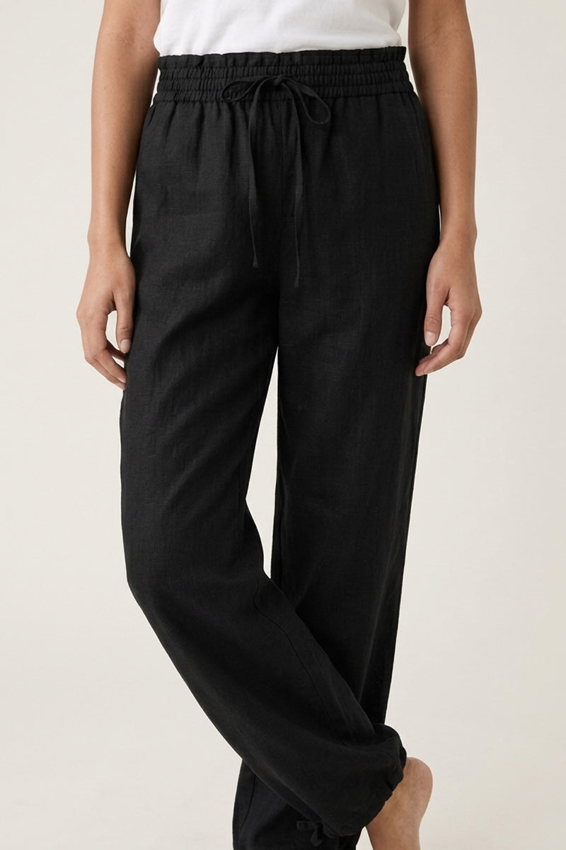 Eine Person trägt eine weite Leinenhose mit Tunnelzug von Princess Goes Hollywood, die elastische Taille und Bündchen an den Knöcheln besitzt. Dazu ein weißes Shirt, Hände entspannt an den Seiten, vor schlicht hellem Hintergrund.