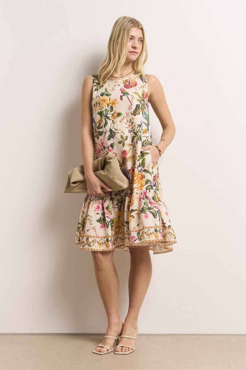 Eine Frau mit langen blonden Haaren trägt ein ärmelloses, knielanges Sommerkleid von Princess Goes Hollywood mit lockerem Schnitt und gerüschtem Saum. Sie trägt eine beigefarbene Clutch und nackte Riemchensandalen und steht vor einer schlichten weißen Wand.