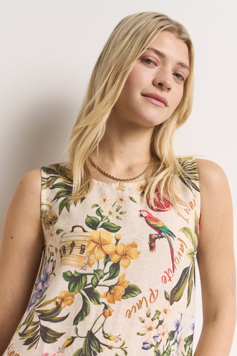 Eine junge Frau mit langen blonden Haaren modelliert ein ärmelloses Princess Goes Hollywood-Top mit tropischem Aufdruck und bunten Blumen und Papageien. Sie lächelt leicht, trägt leichtes Make-up und eine goldene Halskette und steht selbstbewusst vor einem weißen Hintergrund.