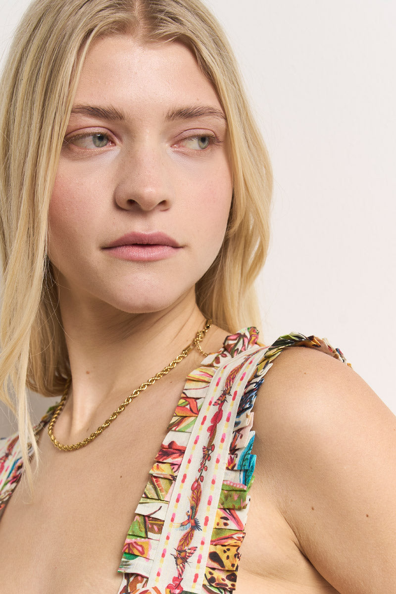 Eine junge, hellhäutige Frau mit langen blonden Haaren blickt zur Seite. Sie trägt eine goldene Kette und ein ärmelloses, mehrfarbiges Baumwoll-Top mit Dschungel-Print und gerüschten Trägern von Princess Goes Hollywood. Ein schlichter Hintergrund unterstreicht ihren nachdenklichen Blick.