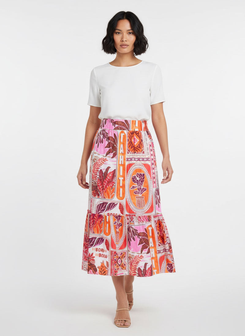 Eine Frau mit gewelltem, kinnlangem Haar trägt ein weißes, kurzärmeliges Oberteil, das in einen Princess Goes Hollywood Midirock aus Baumwollpopeline mit leuchtend roten, orangefarbenen und rosafarbenen Tahiti-Print-Motiven und dem Schriftzug "TAHITI" gesteckt ist. Sie posiert in nackten Riemchenschuhen vor einem schlichten weißen Hintergrund.