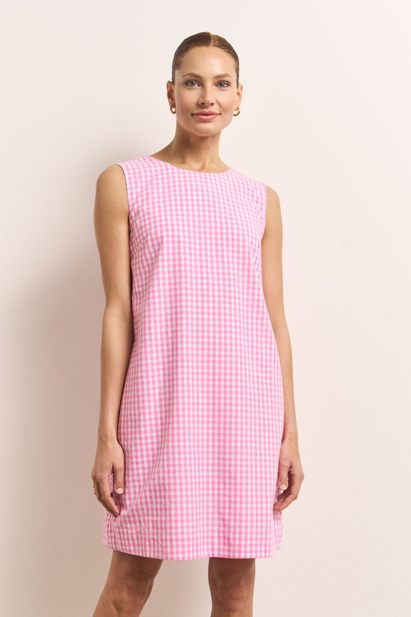 Eine Frau steht an einer hellen Wand und trägt ein ärmelloses, knielanges Princess Goes Hollywood-Minikleid aus Baumwolle mit rosa-weißem Vichy-Karo. Ihr Haar ist zurückgesteckt, sie lächelt sanft und schmückt sich mit kleinen goldenen Reif-Ohrringen.