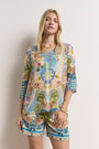 Eine blonde Frau modelliert ein farbenfrohes Set von Princess Goes Hollywood, bestehend aus einem lockeren Oberteil mit strassverzierten Bindebändern und Seidenshorts mit floralen und geometrischen Prints, und posiert vor einer schlichten weißen Wand.